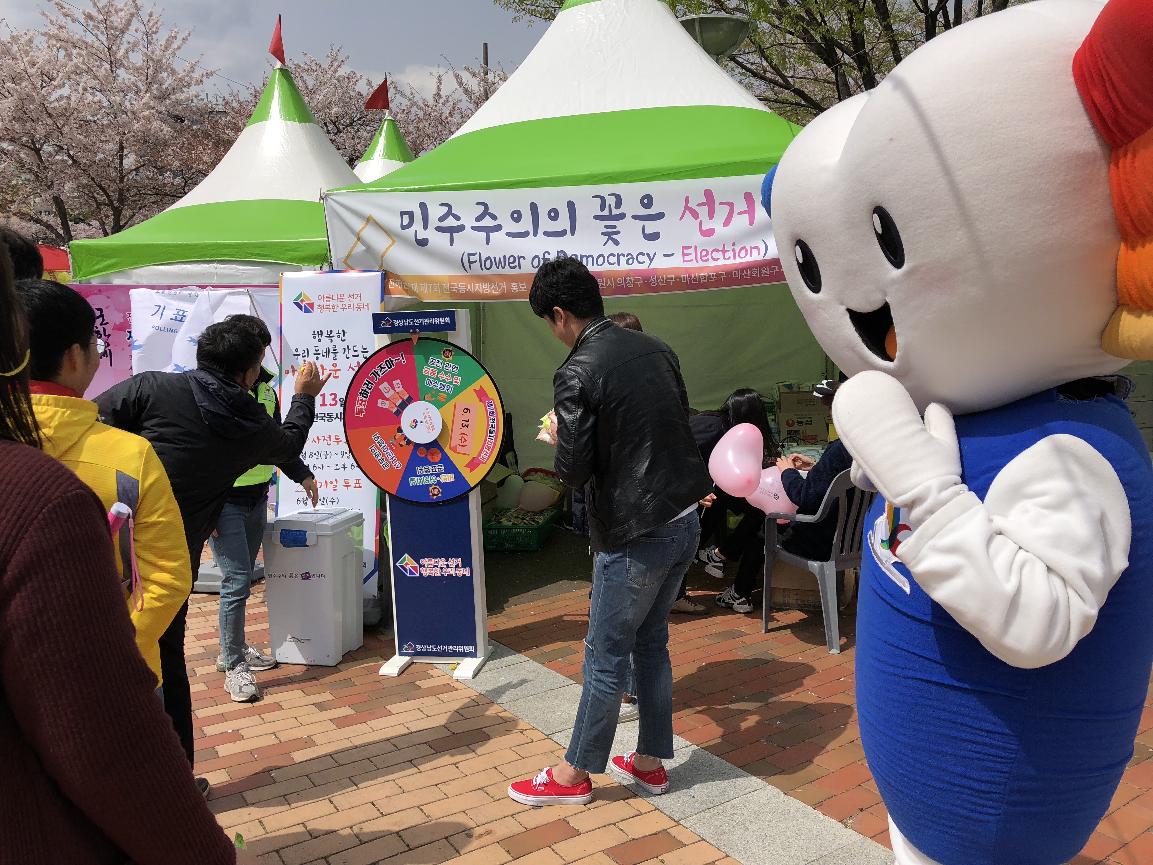 회원구선거관리위원회 직원들과 위원회 캐릭터 '알리'인형이 진해군항제에서 시민들을 대상으로 홍보부스를 운영하고 있는 모습입니다