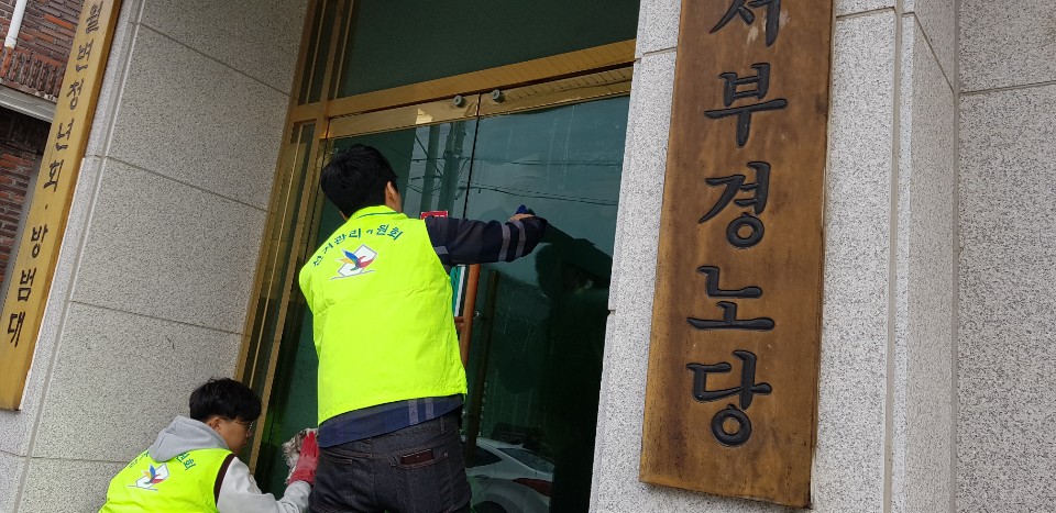 관리주임과 공정선거지원단이 마을회관 현관문을 닦는 모습입니다.